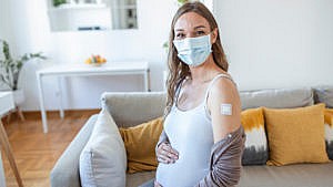 a photo of a woman touching her pregnant belly showing her vaccine bandaid