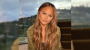 Chrissy Teigen posing while sitting in front of a window