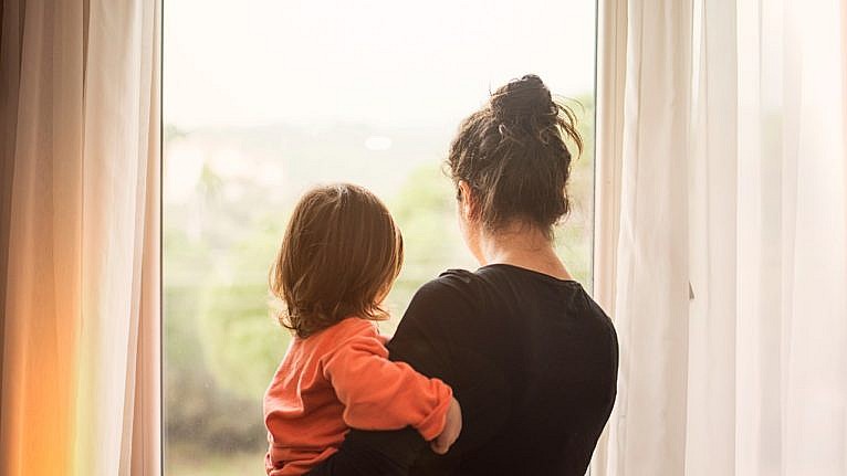 An image of a mother holding her child while looking out of a window.