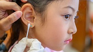 An image of a girl from the side with someone holding a q-tip to her ear next to an earring.