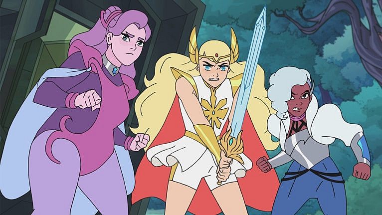 An image of the cartoon She-Ra and the Princesses of Power; one character is purple, another is blonde holding a sword, and the third has gray hair, wearing blue.