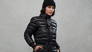 A woman wearing a puffy down snow suit and a black toque with her hands in her pockets.