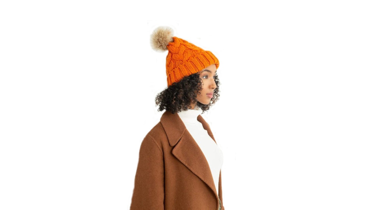 An image of a woman wearing an orange toque with a beige pom on the top.