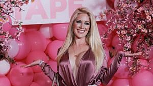 Heidi Montag smiles, wearing a bright pink silk shirt and standing in front of pink balloons.