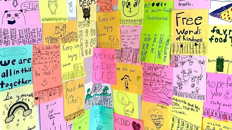 A poster board is covered with neon paper with childrens' writing on it to celebrate the new hotline.