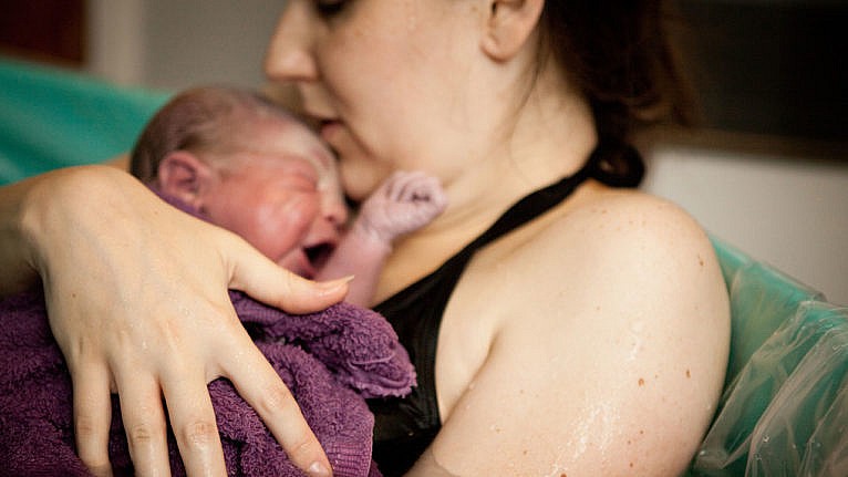 A mother cradles her newborn baby while lying in the tub after a water birth