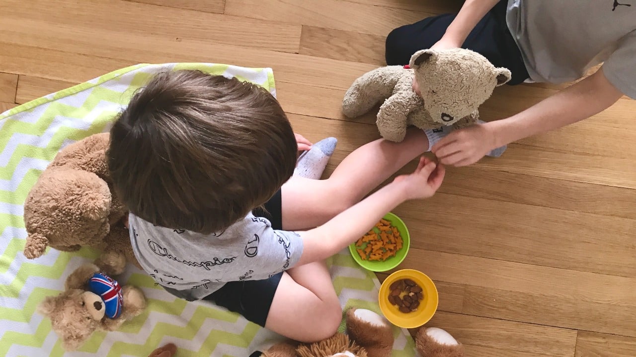 An image of two young boys playing together on the floor with a teddy bear.