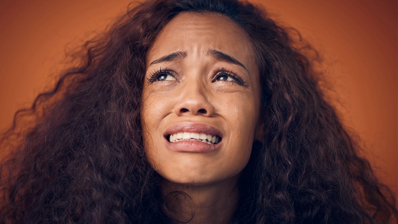 A woman with curly hair crying with a pained expression on her face.