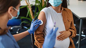 A pregnant person getting a vaccine while wearing a face mask
