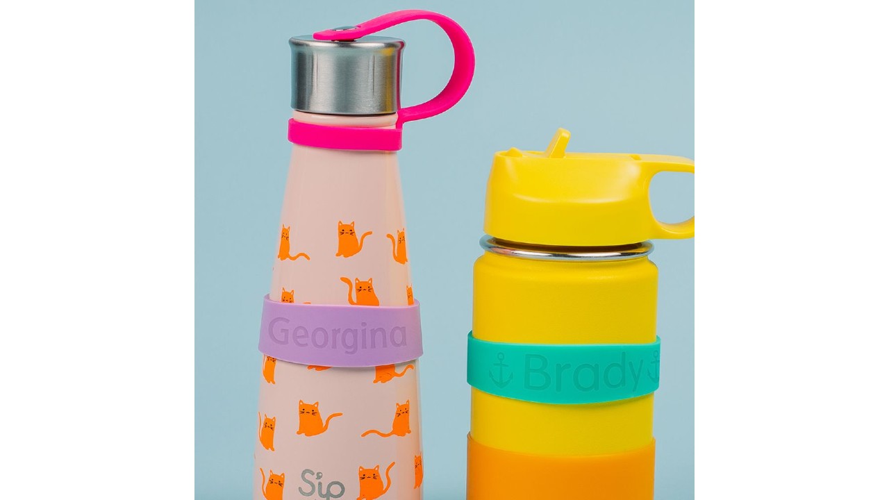 An image of a pink water bottle with orange cats on the left and a yellow and orange water bottle on the right. The left has a purple label with the name Georgina and the right has a turquoise label with the name Brady.