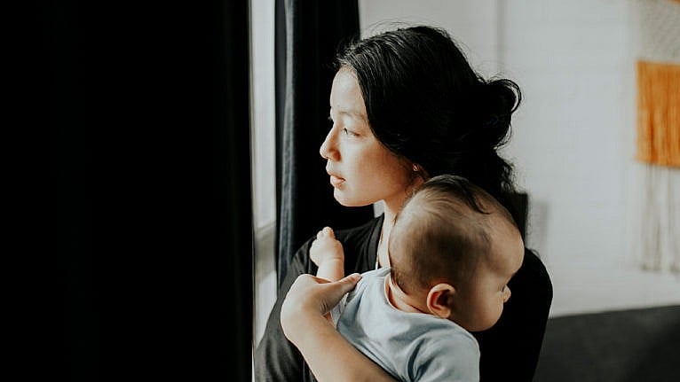 A mom looking out the window while holding their baby