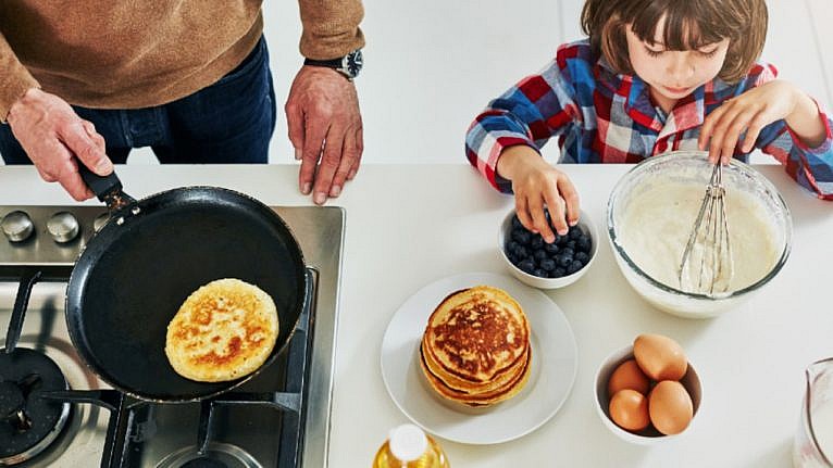High angle shot of a child making pancakes with his father who is cooking them on a gas stove