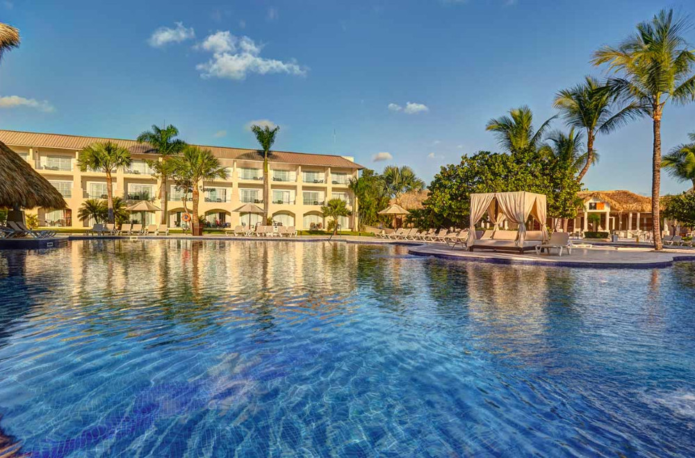A pool with lounge chairs and booths surrounding it, with the hotel in the background at Royalton Splash Punta Cana