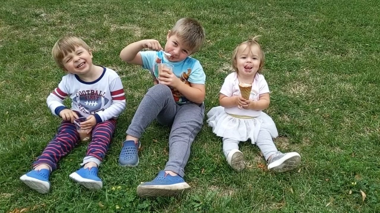 Three kids sitting together on the grass outdoors