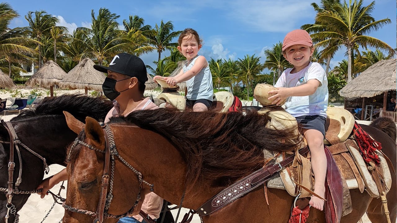 Two kindergarteners ride horses on the beach