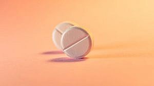 Two round white pills on a plain orange-pink background
