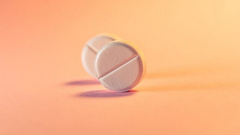 Two round white pills on a plain orange-pink background