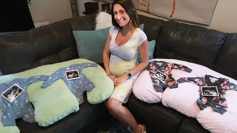 Ashley with four ultrasound photos sitting on four sets of baby clothes