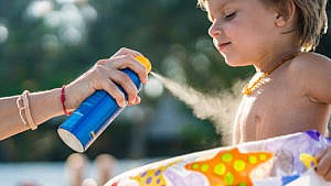A caregiver applies spray sunscreen to a boy at an outdoor pool