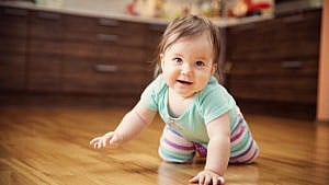 A baby smiling and crawling in the kitchen
