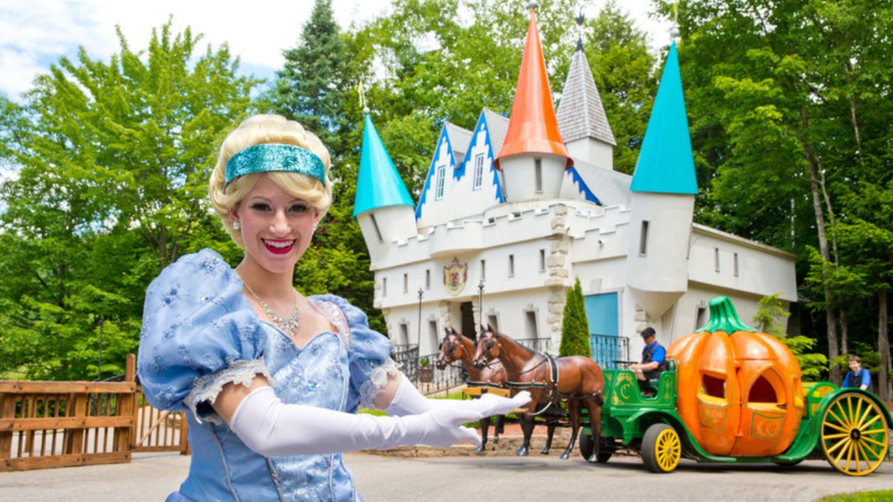 Cindarella, with a pumpkin carriage with horses and castle in the background, at Story Land in New Hampshire