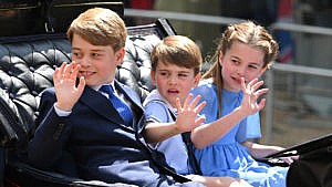Prince George, Prince Louis and Princess Charlotte sit in a row in a carriage waving to crowds during the Trooping the Colour celebrations