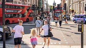 Mom and two children crossing a busy street in central London with double decker buses in the background