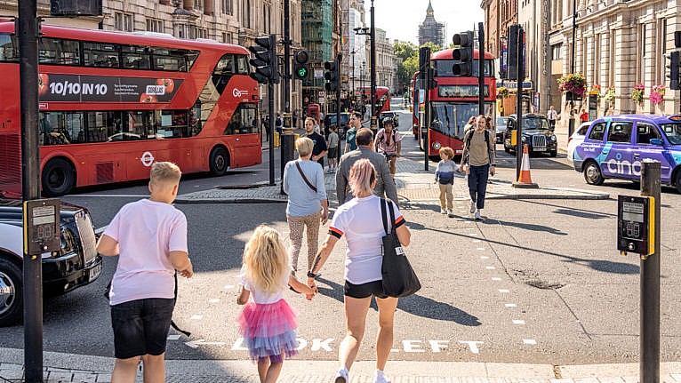 Mom and two children crossing a busy street in central London with double decker buses in the background