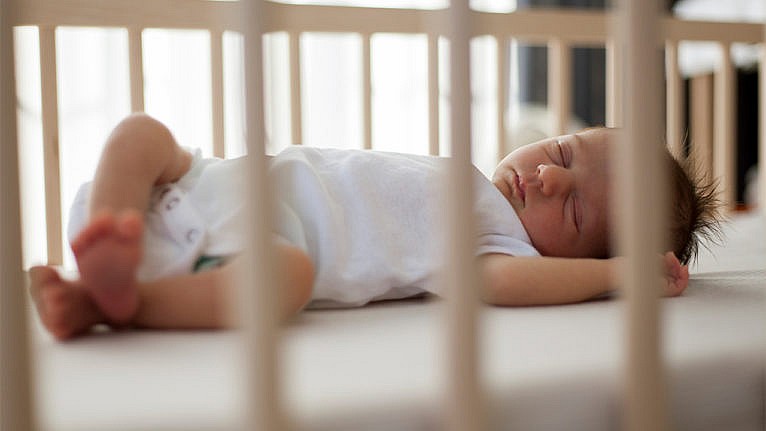 An infant sleeps on a bare crib.