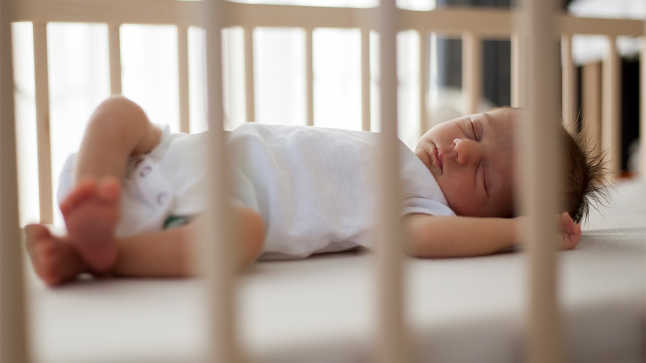 An infant sleeps on a bare crib.