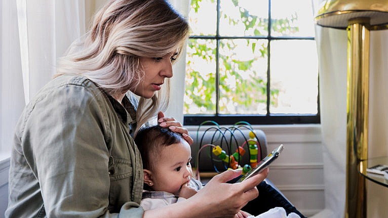A mom with her baby scrolling through social media on her phone. Moms are being targeted by vaccine misinformation