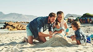 A family builds a mound of sand together while playing on the beach.