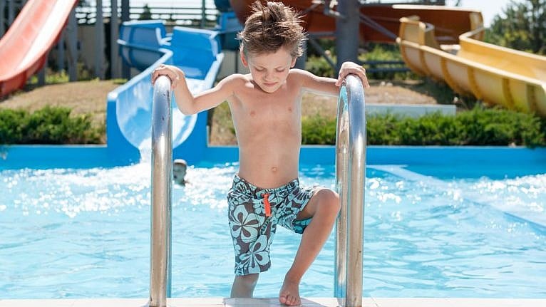 Little boy climbing out of a pool while looking down at his swim shorts