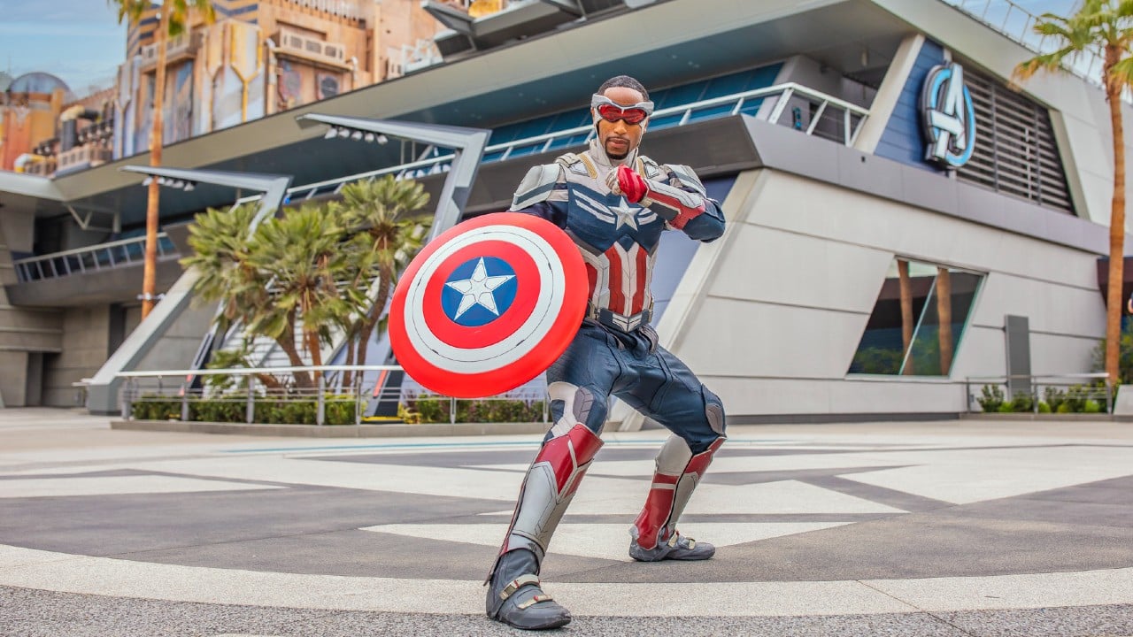 Captain America holding his shield and standing before the Avengers Campus building