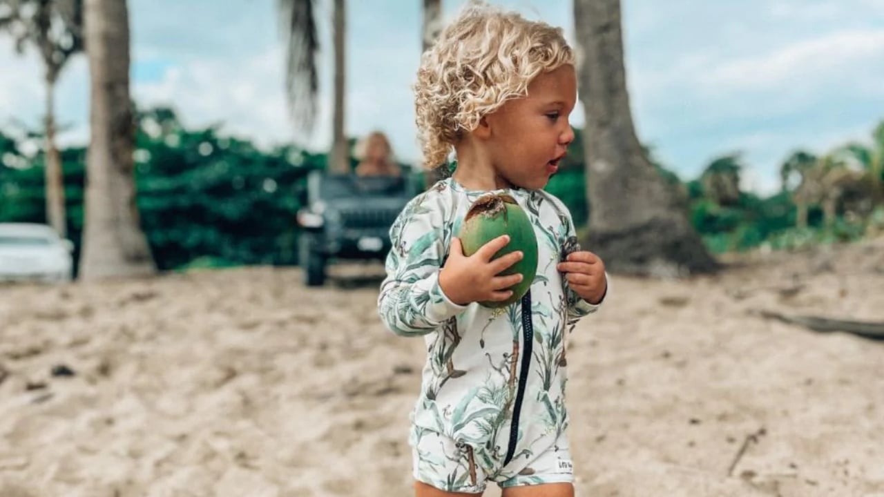 A kid on the beach wearing a gender-neutral rashguard made by Little Yogi