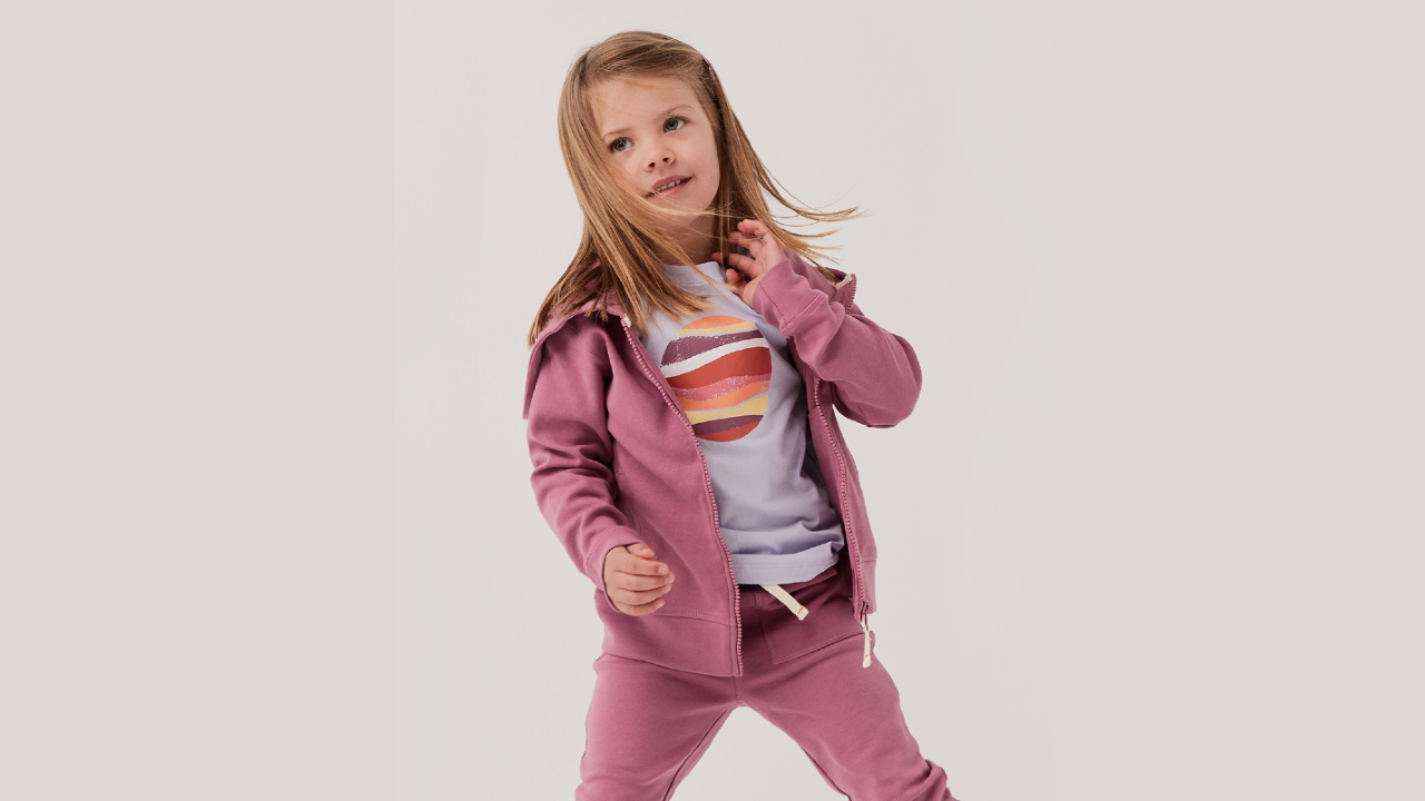 A child models a gender neutral Pact t-shirt and tracksuit