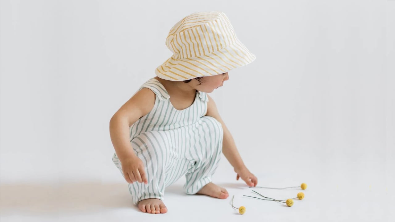 A child models a neutral hat and jumpsuit from Pehr