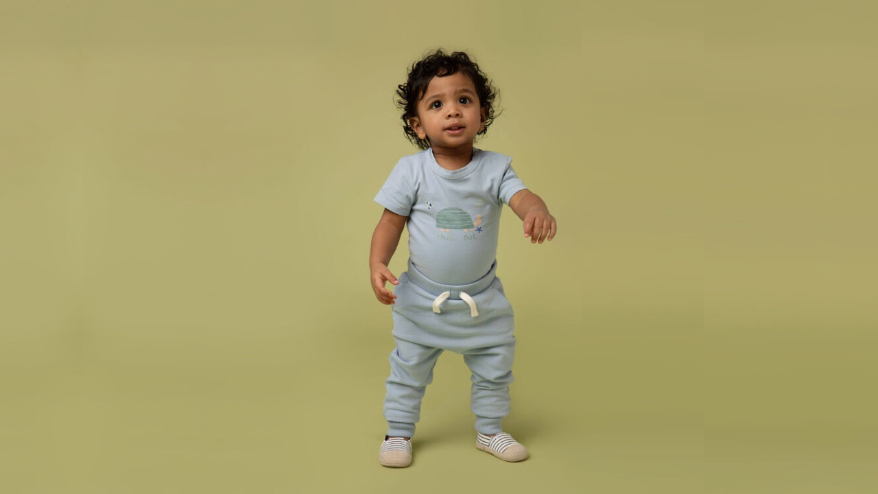 A child models gender-neutral sweatpants, shoes and a t-shirt from Rise Little Earthling