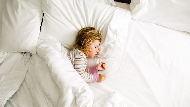 Little girl sleeping on a big bed with white sheets and duvet