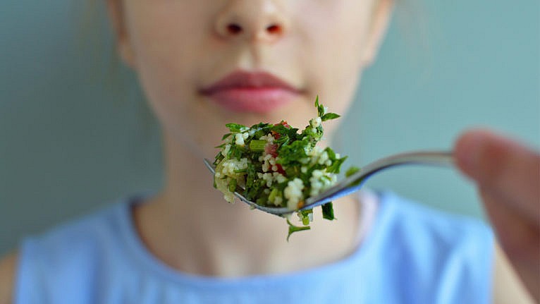 a tween girl being fed a spoon full of quinoa salad