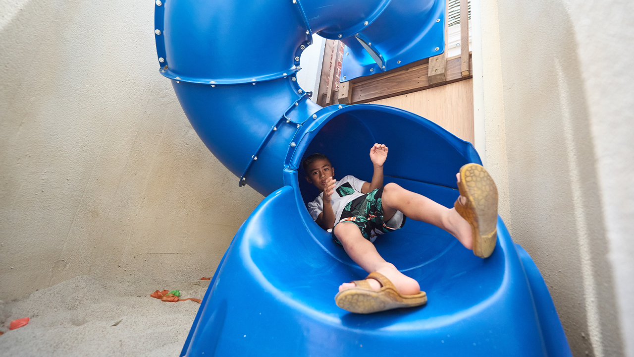 A kid slides down a twisty slide the leads into a sand box.