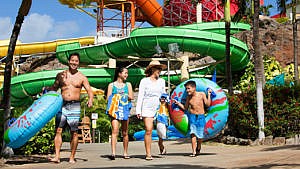 A family walks through a water park together while carrying inner tube floaties and towels