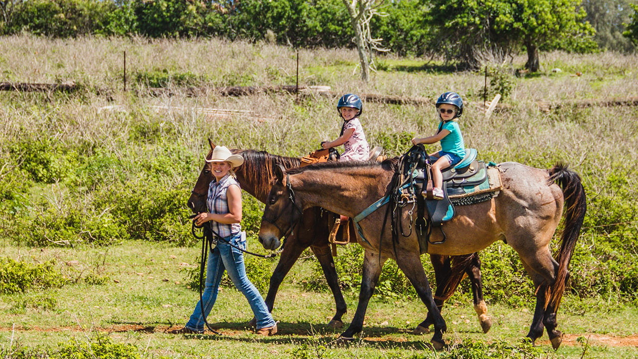Two kids ride ponies that are being led by an adult.
