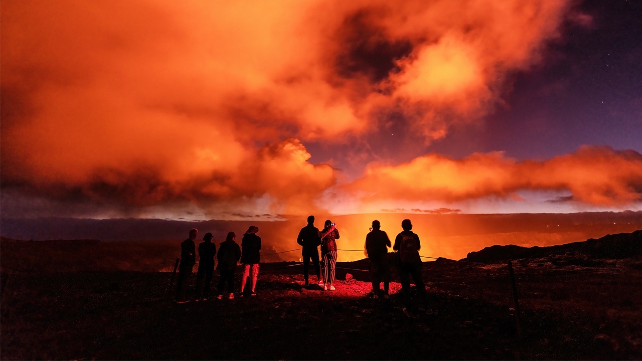 Visitors to the Hawaii Volcanoes National Park watch the glow of a volcanic eruption