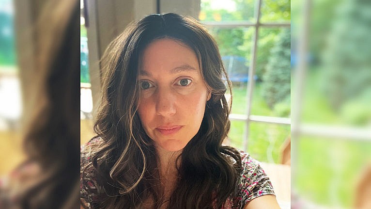 A mom takes a selfie while wearing a wig of thick brown wavy hair.