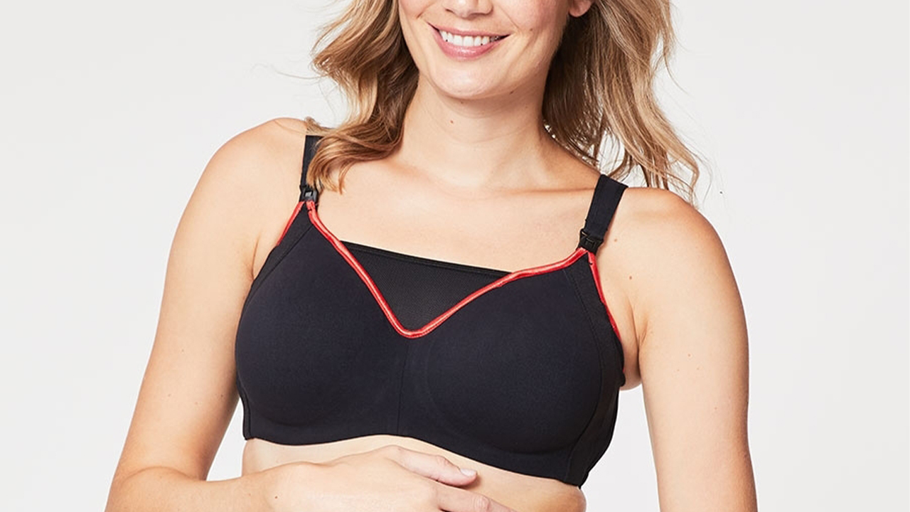 A woman wearing a black nursing sports bra with a neon pink piping edge