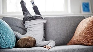 A child lying face down on the sofa as if they just collapsed in exhaustion.