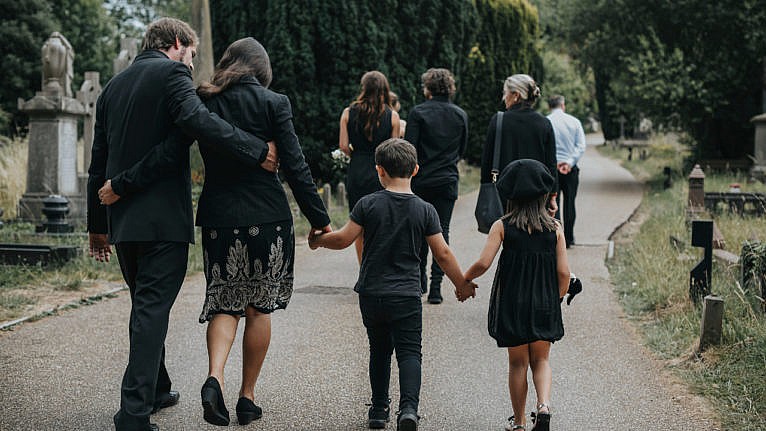 A family of four dressed in all black walks down a path leading to a cemetery.
