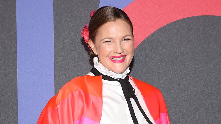 Drew Barrymore smiling on a red carpet wearing a brightly coloured jacket.