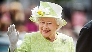 The Queen smiles and waves wearing a lime green suit and hat.